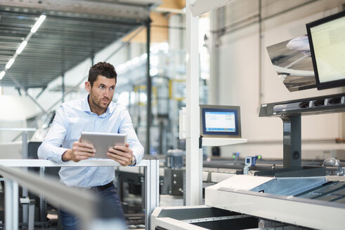 Geschäftsmann mit Tablet und Blick auf eine Maschine in einer modernen Fabrik - DIGF03705