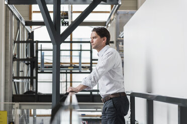 Businessman standing at railing in factory thinking - DIGF03709