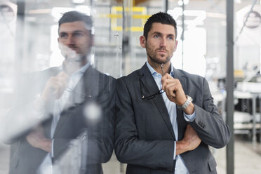 Businessman leaning against glass pane in modern factory thinking - DIGF03718