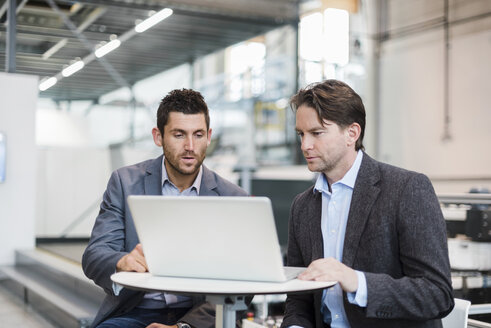 Zwei Geschäftsleute teilen sich einen Laptop in einer Fabrik - DIGF03723