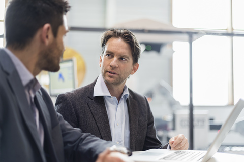 Two businessmen sharing laptop in factory stock photo