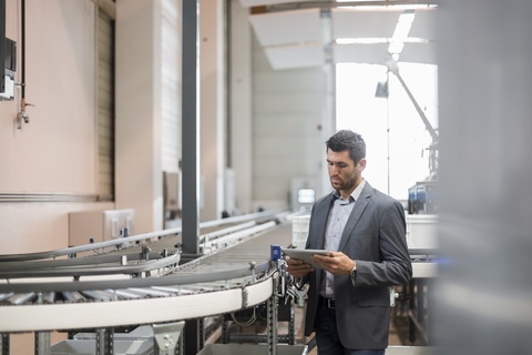 Businessman using tablet at conveyor belt in factory stock photo