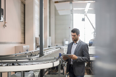 Businessman using tablet at conveyor belt in factory - DIGF03733