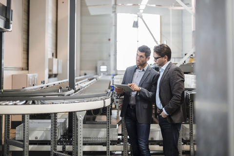 Two businessmen with tablet talking at conveyor belt in factory stock photo