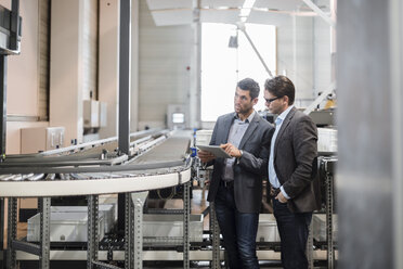 Two businessmen with tablet talking at conveyor belt in factory - DIGF03734