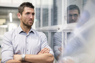 Businessman at glass pane in modern factory thinking - DIGF03741