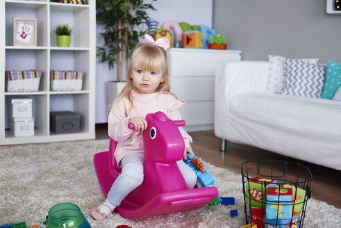 Porträt eines kleinen Mädchens, das auf einem rosa Schaukelpferd im Wohnzimmer sitzt - ABIF00257