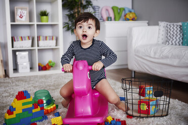 Porträt eines kleinen Jungen, der auf einem rosa Schaukelpferd im Wohnzimmer sitzt - ABIF00264