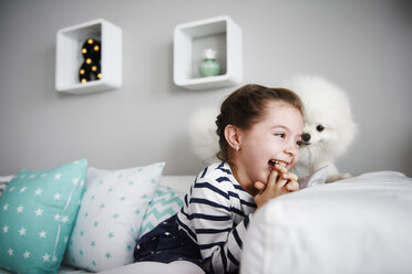 Lachendes kleines Mädchen spielt mit Hund auf der Couch im Wohnzimmer - ABIF00268