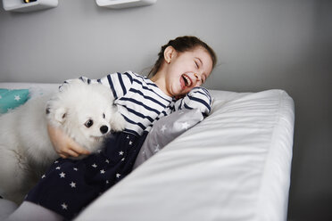 Lachendes kleines Mädchen spielt mit Hund auf der Couch im Wohnzimmer - ABIF00269