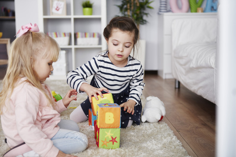 Zwei kleine Mädchen spielen zu Hause auf dem Teppich mit Bauklötzen, lizenzfreies Stockfoto