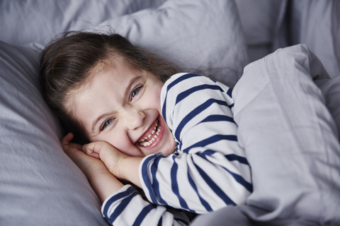 Porträt eines lachenden kleinen Mädchens, das im Bett liegt, lizenzfreies Stockfoto