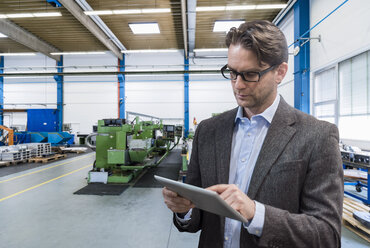 Businessman using tablet on factory shop floor - DIGF03758