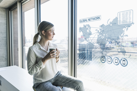 Junge Geschäftsfrau, die eine virtuelle Weltkarte an der Fensterscheibe im Büro betrachtet, lizenzfreies Stockfoto