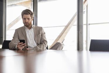 Businessman using cell phone in conference room - DIGF03761