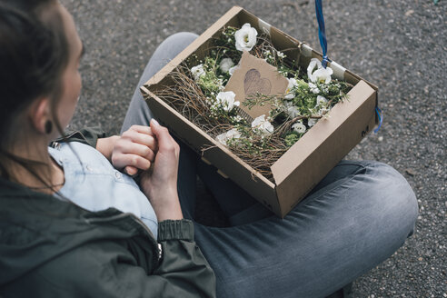 Frau mit Blumenarrangement im Karton auf dem Boden sitzend - GUSF00605