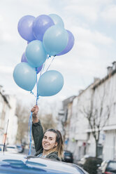 Portrait of smiling woman with blue balloons on the street - GUSF00617