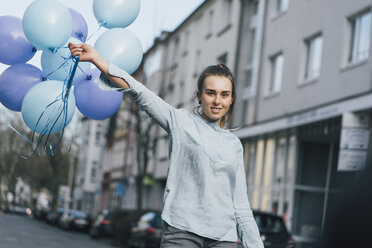 Porträt einer lächelnden Frau mit blauen Luftballons auf der Straße - GUSF00620