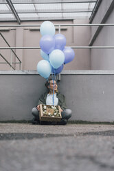 Lächelnde Frau mit Blumen in einer Pappschachtel und blauen Luftballons auf dem Boden sitzend - GUSF00621