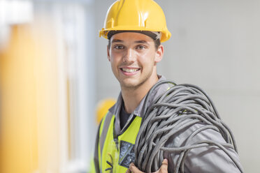 Porträt eines lächelnden Elektrikers mit Kabel auf einer Baustelle - ZEF15365