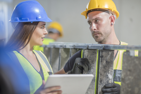 Woman with tablet talking to man with ladder on construction site stock photo
