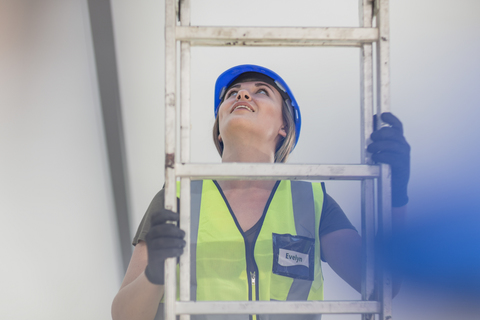 Young woman on construction site climbing ladder stock photo