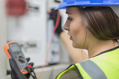 Junge Elektrikerin bei der Arbeit mit einem Voltmeter am Sicherungskasten - ZEF15373