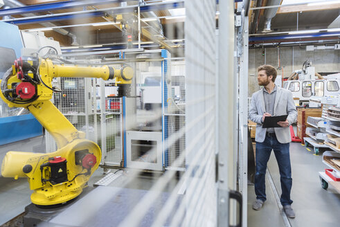 Businessman looking at industrial robot in modern factory - DIGF03832