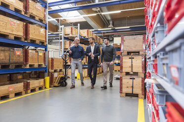 Three men walking and talking in factory storeroom - DIGF03848