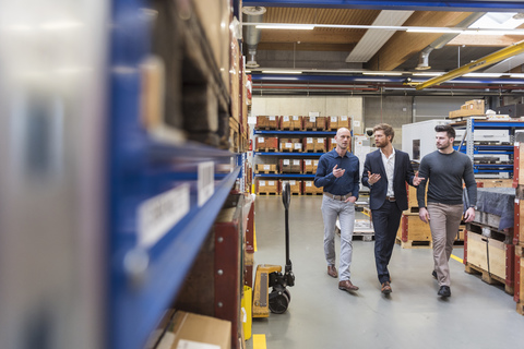 Drei Männer gehen und sprechen in einem Lagerraum einer Fabrik, lizenzfreies Stockfoto