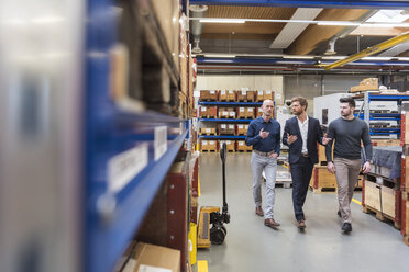 Three men walking and talking in factory storeroom - DIGF03849