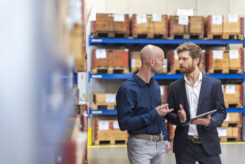 Zwei Geschäftsleute mit Tablet im Gespräch im Lagerraum einer Fabrik - DIGF03851