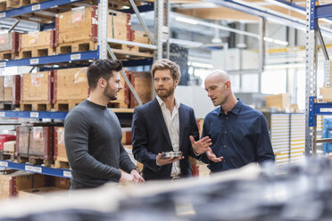 Three men talking in factory storeroom - DIGF03857