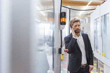 Geschäftsmann am Mobiltelefon an einer Maschine in einer modernen Fabrik - DIGF03870