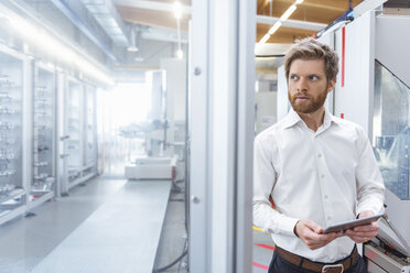 Businessman with tablet looking at machine in modern factory - DIGF03874