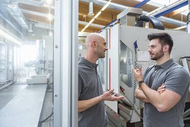 Zwei Männer diskutieren an einer Maschine in einer modernen Fabrik - DIGF03875