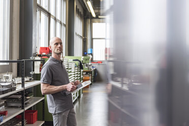 Mann steht in einer modernen Fabrik und hält ein Produkt - DIGF03878