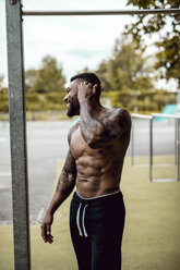 Tattooed bodybuilder standing on sports field - DAWF00592