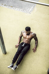 Tattooed physical athlete doing muscle training on ground of sports field - DAWF00598