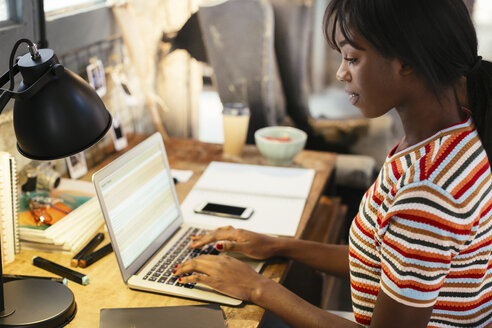 Junge Frau sitzt am Schreibtisch und arbeitet am Laptop - EBSF02280