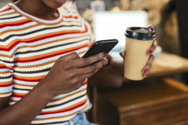 Frau hält Kaffee zum Mitnehmen in der Hand und benutzt ein Smartphone, Nahaufnahme - EBSF02288