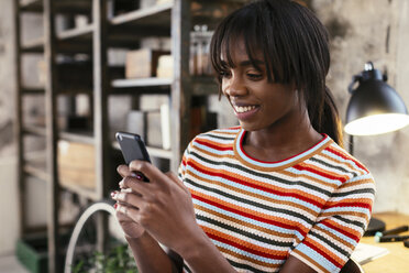 Portrait of smiling young woman in a loft using cell phone - EBSF02289