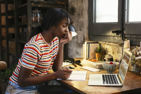 Nachdenkliche junge Frau sitzt am Schreibtisch in einem Loft und schaut auf einen Laptop - EBSF02291