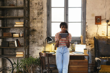 Junge Frau steht vor einem Schreibtisch in einem Loft und benutzt ein Tablet - EBSF02292