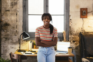 Portrait of smiling young woman standing front of desk in a loft - EBSF02293