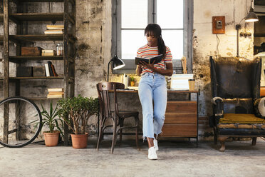 Junge Frau steht vor einem Schreibtisch in einem Loft und benutzt ein Notizbuch - EBSF02294