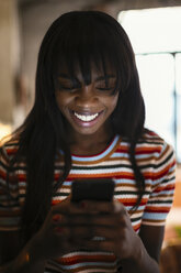 Porträt einer glücklichen jungen Frau, die auf ihr Mobiltelefon schaut - EBSF02304