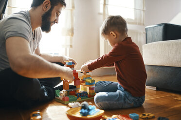 Vater und Sohn sitzen auf dem Boden und spielen zusammen mit Bauklötzen - ZEDF01276