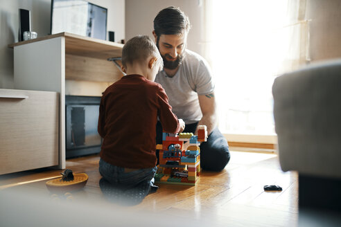 Father and son sitting on the floor at home playing together with building bricks - ZEDF01277