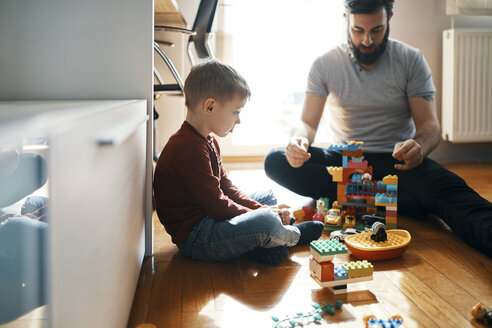 Father playing with building bricks on the floor at home ignoring his sad little son sitting beside him - ZEDF01278